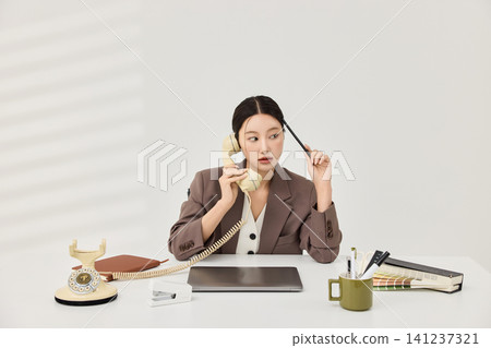 Professional woman talking on a vintage telephone at her desk Professional woman talking on a vintage telephone at her desk 141237321