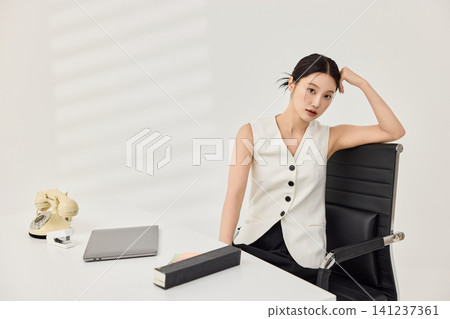 Asian businesswoman in a white vest reviewing documents at her desk Asian businesswoman in a white vest reviewing documents at her desk 141237361