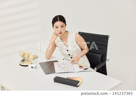 Female designer working with a laptop and printed materials Female designer working with a laptop and printed materials 141237365