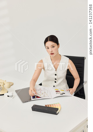 Asian businesswoman in a white vest reviewing documents at her desk Asian businesswoman in a white vest reviewing documents at her desk 141237368