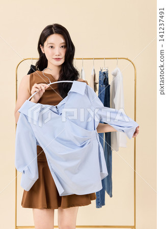 Woman smiling between hanging clothes in a dressing room Woman smiling between hanging clothes in a dressing room 141237491