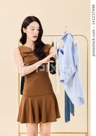 Surprised woman looking at clothes while styling an outfit Surprised woman looking at clothes while styling an outfit 141237496