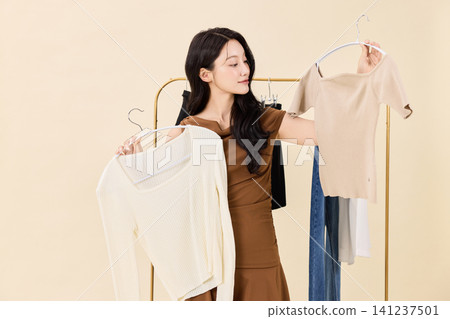 Woman smiling between hanging clothes in a dressing room Woman smiling between hanging clothes in a dressing room 141237501