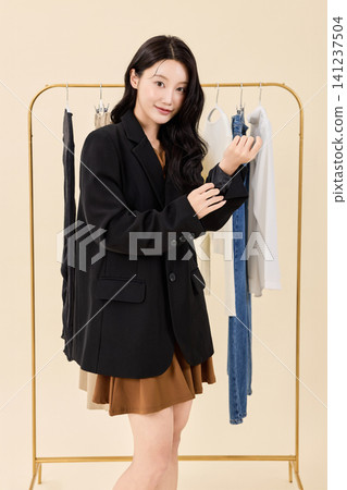 Woman smiling between hanging clothes in a dressing room Woman smiling between hanging clothes in a dressing room 141237504
