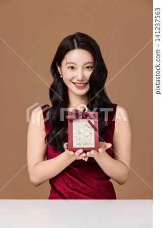 Elegant Asian woman presenting a wrapped gift box Elegant Asian woman presenting a wrapped gift box 141237563
