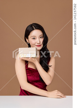 Elegant Asian woman presenting a wrapped gift box Elegant Asian woman presenting a wrapped gift box 141237582