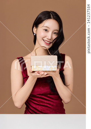 Smiling woman showing a ribbon-wrapped present in a studio Smiling woman showing a ribbon-wrapped present in a studio 141237584