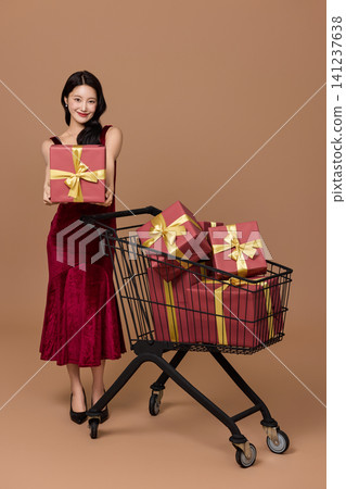 Asian woman pushing a shopping cart filled with wrapped gifts 141237638