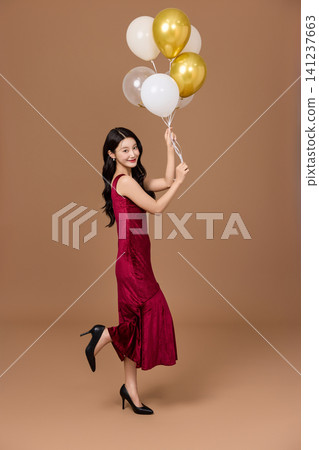 Asian woman in a red dress posing with party balloons Asian woman in a red dress posing with party balloons 141237663