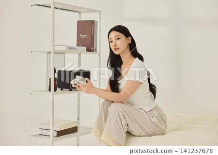 Young Asian woman relaxing on a cream bed in a bright bedroom Young Asian woman relaxing on a cream bed in a bright bedroom 141237678