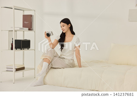 Woman sitting on a bed beside a modern white shelving unit Woman sitting on a bed beside a modern white shelving unit 141237681