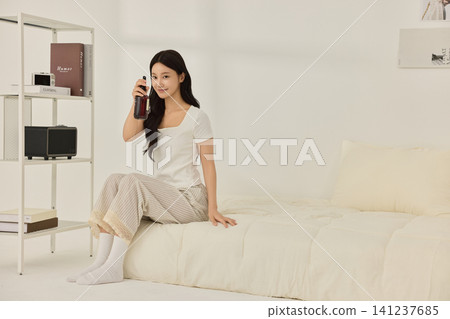 Woman sitting on a bed beside a modern white shelving unit Woman sitting on a bed beside a modern white shelving unit 141237685