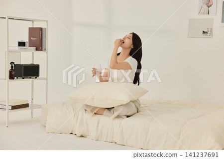 Asian woman sitting in bed with a glass of water Asian woman sitting in bed with a glass of water 141237691