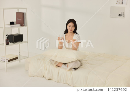Young Asian woman drinking water on a bed in the morning Young Asian woman drinking water on a bed in the morning 141237692