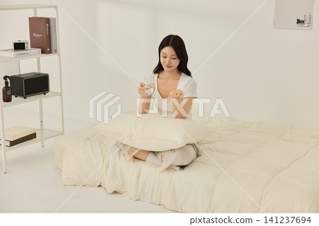 Woman taking a supplement with water in a bright bedroom Woman taking a supplement with water in a bright bedroom 141237694
