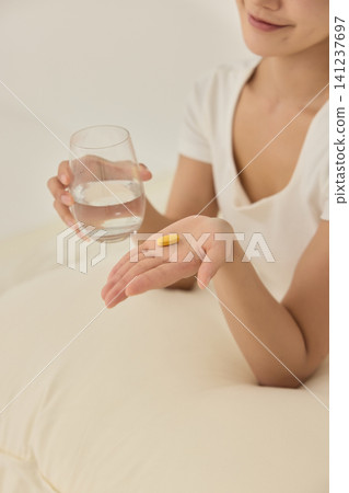 Woman taking a supplement with water in a bright bedroom Woman taking a supplement with water in a bright bedroom 141237697