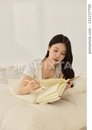 Young Asian woman reading a book while lying on a cream bed Young Asian woman reading a book while lying on a cream bed 141237700