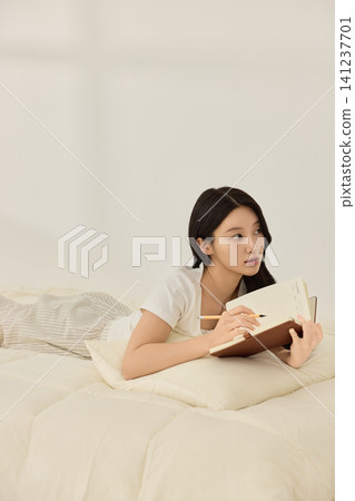 Woman writing in a notebook on a bright bedroom bed Woman writing in a notebook on a bright bedroom bed 141237701