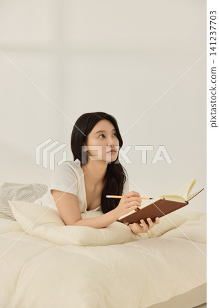 Young Asian woman reading a book while lying on a cream bed Young Asian woman reading a book while lying on a cream bed 141237703