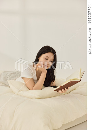 Asian woman enjoying quiet reading time in a bedroom Asian woman enjoying quiet reading time in a bedroom 141237704