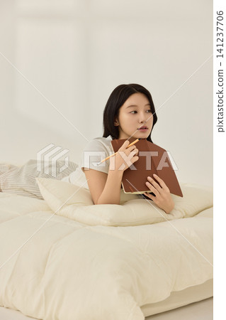 Woman writing in a notebook on a bright bedroom bed Woman writing in a notebook on a bright bedroom bed 141237706