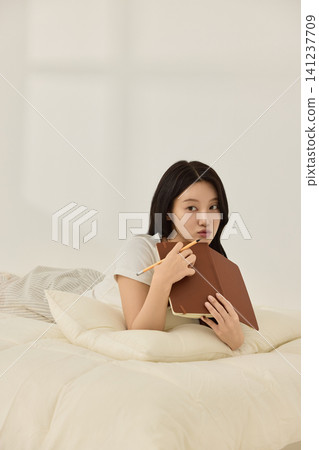 Asian woman enjoying quiet reading time in a bedroom Asian woman enjoying quiet reading time in a bedroom 141237709