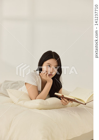 Young Asian woman reading a book while lying on a cream bed Young Asian woman reading a book while lying on a cream bed 141237710