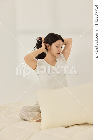Relaxed woman tying her hair after waking up in a bedroom Relaxed woman tying her hair after waking up in a bedroom 141237714