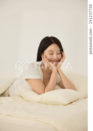 Asian woman lying on a bed and reaching toward an alarm clock Asian woman lying on a bed and reaching toward an alarm clock 141237726