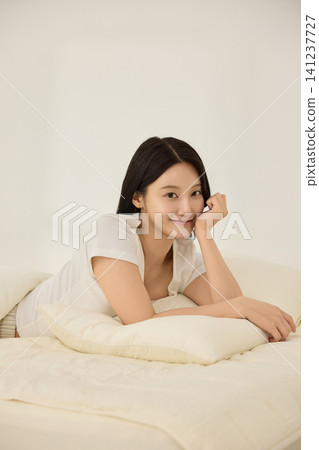 Young Asian woman smiling on a bed with an alarm clock Young Asian woman smiling on a bed with an alarm clock 141237727