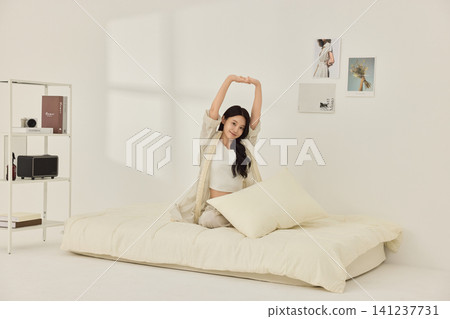Woman sitting on a bed with pillows during a morning routine Woman sitting on a bed with pillows during a morning routine 141237731