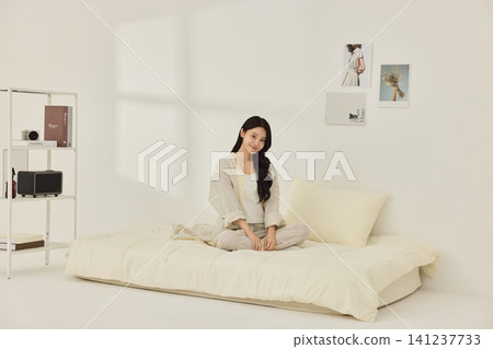 Asian woman holding a pillow while relaxing on a bed 141237733