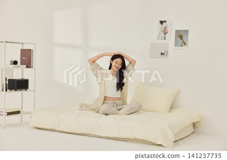 Young Asian woman stretching on a cream bed in a bright bedroom 141237735