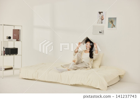 Young Asian woman stretching on a cream bed in a bright bedroom 141237743
