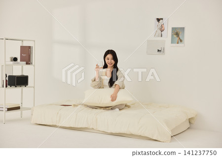Asian woman holding a pillow while relaxing on a bed 141237750