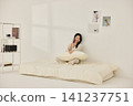 Woman sitting on a bed with pillows during a morning routine 141237751
