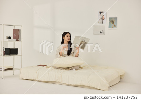 Young Asian woman stretching on a cream bed in a bright bedroom Young Asian woman stretching on a cream bed in a bright bedroom 141237752