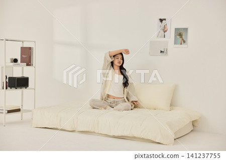 Young Asian woman stretching on a cream bed in a bright bedroom Young Asian woman stretching on a cream bed in a bright bedroom 141237755