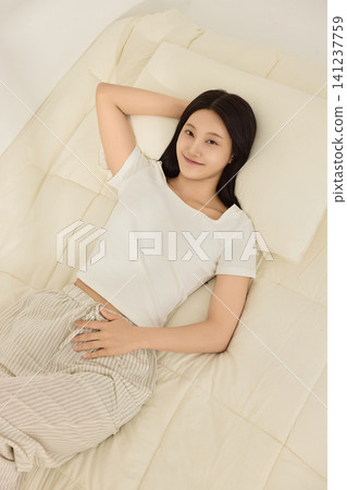 Asian woman smiling under bedding during a cozy morning Asian woman smiling under bedding during a cozy morning 141237759