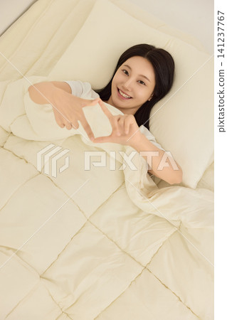 Asian woman smiling under bedding during a cozy morning Asian woman smiling under bedding during a cozy morning 141237767