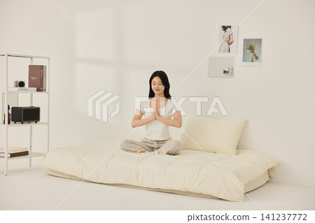Woman relaxing with a pillow in a bright white bedroom Woman relaxing with a pillow in a bright white bedroom 141237772