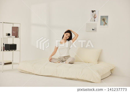 Calm home lifestyle with a woman stretching on a cream bed Calm home lifestyle with a woman stretching on a cream bed 141237773