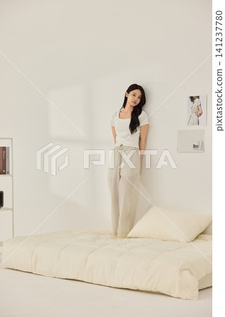 Woman stretching with a pillow in a bright minimal bedroom Woman stretching with a pillow in a bright minimal bedroom 141237780