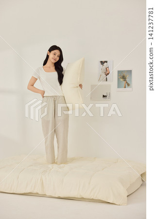 Young Asian woman standing on a bed and holding a large pillow Young Asian woman standing on a bed and holding a large pillow 141237781