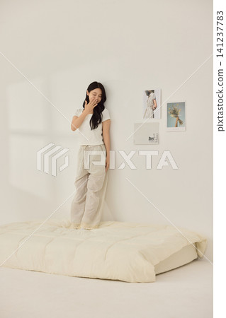 Asian woman posing with a pillow in a white bedroom Asian woman posing with a pillow in a white bedroom 141237783
