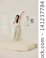Young Asian woman standing on a bed and holding a large pillow 141237784