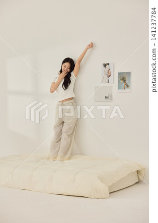 Young Asian woman standing on a bed and holding a large pillow 141237784