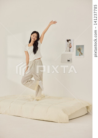 Woman stretching with a pillow in a bright minimal bedroom Woman stretching with a pillow in a bright minimal bedroom 141237785