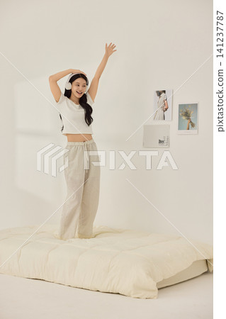Asian woman posing with a pillow in a white bedroom Asian woman posing with a pillow in a white bedroom 141237787