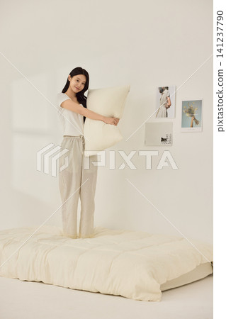 Asian woman posing with a pillow in a white bedroom 141237790